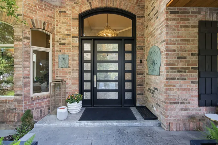 Brick exterior with arched detailing, black framed multi-pane entry door, transom window, and stone-finish porch