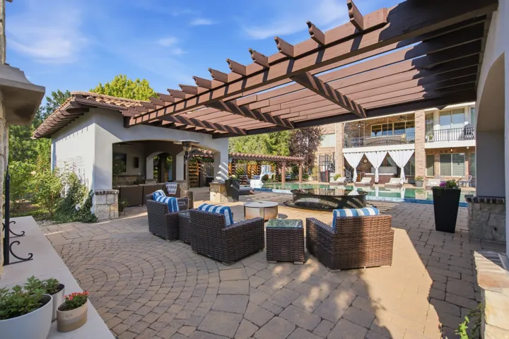 Expansive paver patio with a wood pergola, outdoor kitchen, and pool with an integrated spa