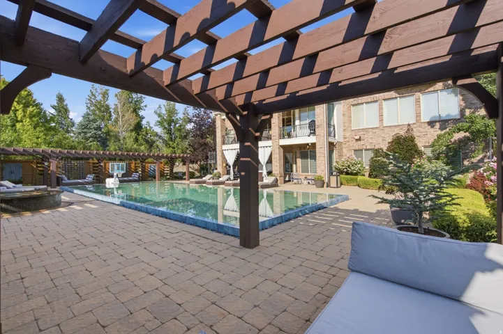Expansive paver patio with a swimming pool, multiple pergolas, and a brick exterior residence