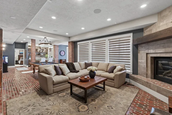 Open-concept living area with brick-finish flooring, recessed lighting, and a stone-clad fireplace featuring a wood mantel