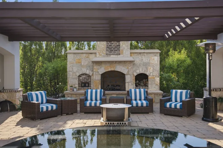 Covered outdoor patio featuring a stone fireplace, brick accents, and a paved surface