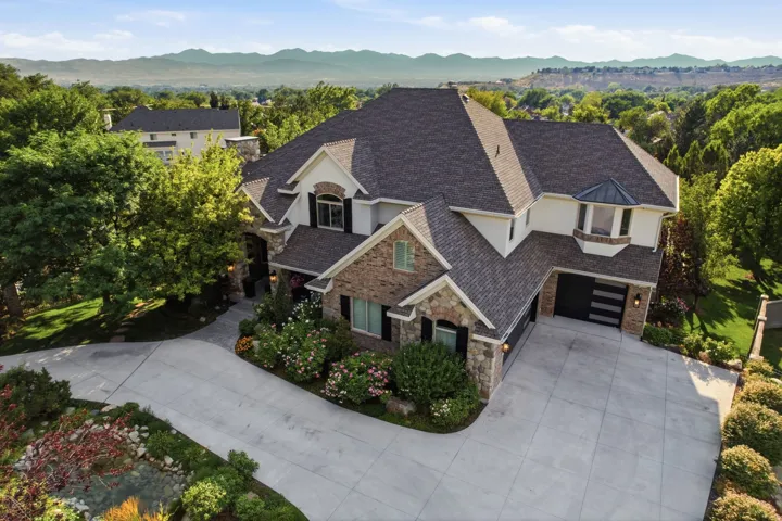 Stately exterior featuring stone and stucco finishes, an attached three-car garage, mature landscaping, and an expansive paved driveway