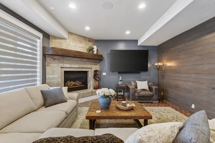 Built-in fireplace with a stone surround and wood mantle, shiplap accent wall, recessed lighting, and wood-finish flooring