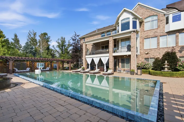 Expansive paver patio with a rectangular swimming pool, integrated pergola, and a tiered fountain