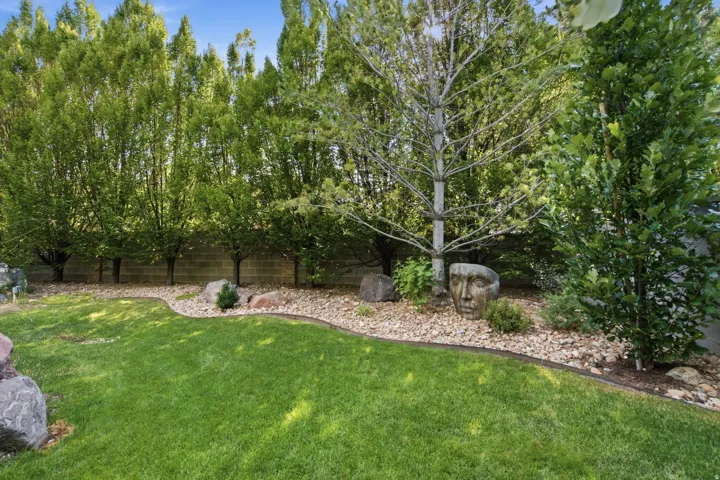 Manicured lawn with a curved landscape bed featuring decorative rocks, mature trees, and a concrete block retaining wall