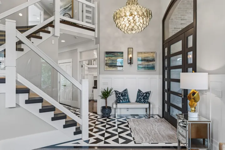 Grand entry featuring a modern chandelier, dark-framed glass paneled door, and a staircase with glass panel railings