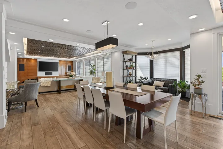 Expansive open-concept living area featuring wood-finish flooring, recessed lighting, a bay window with plantation shutters, and a distinctive textured ceiling accent