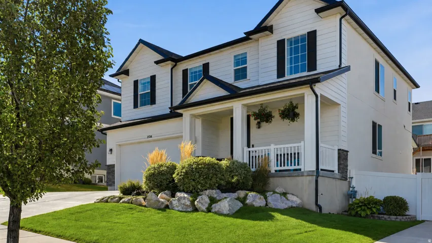 Two-story residence featuring a covered front porch, white siding, black window shutters, and an attached garage
