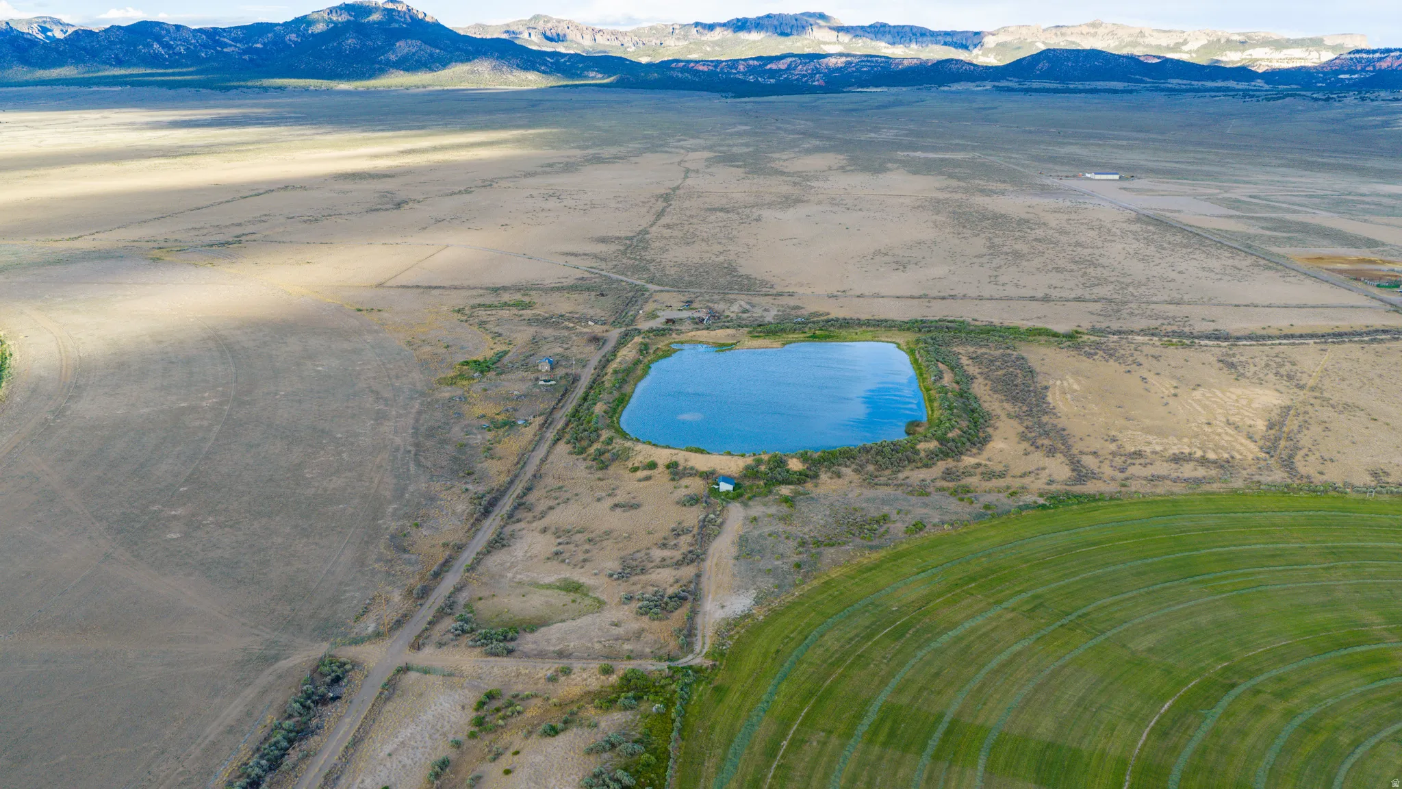 Expansive land parcel featuring a natural pond, cultivated fields, and distant mountain ranges