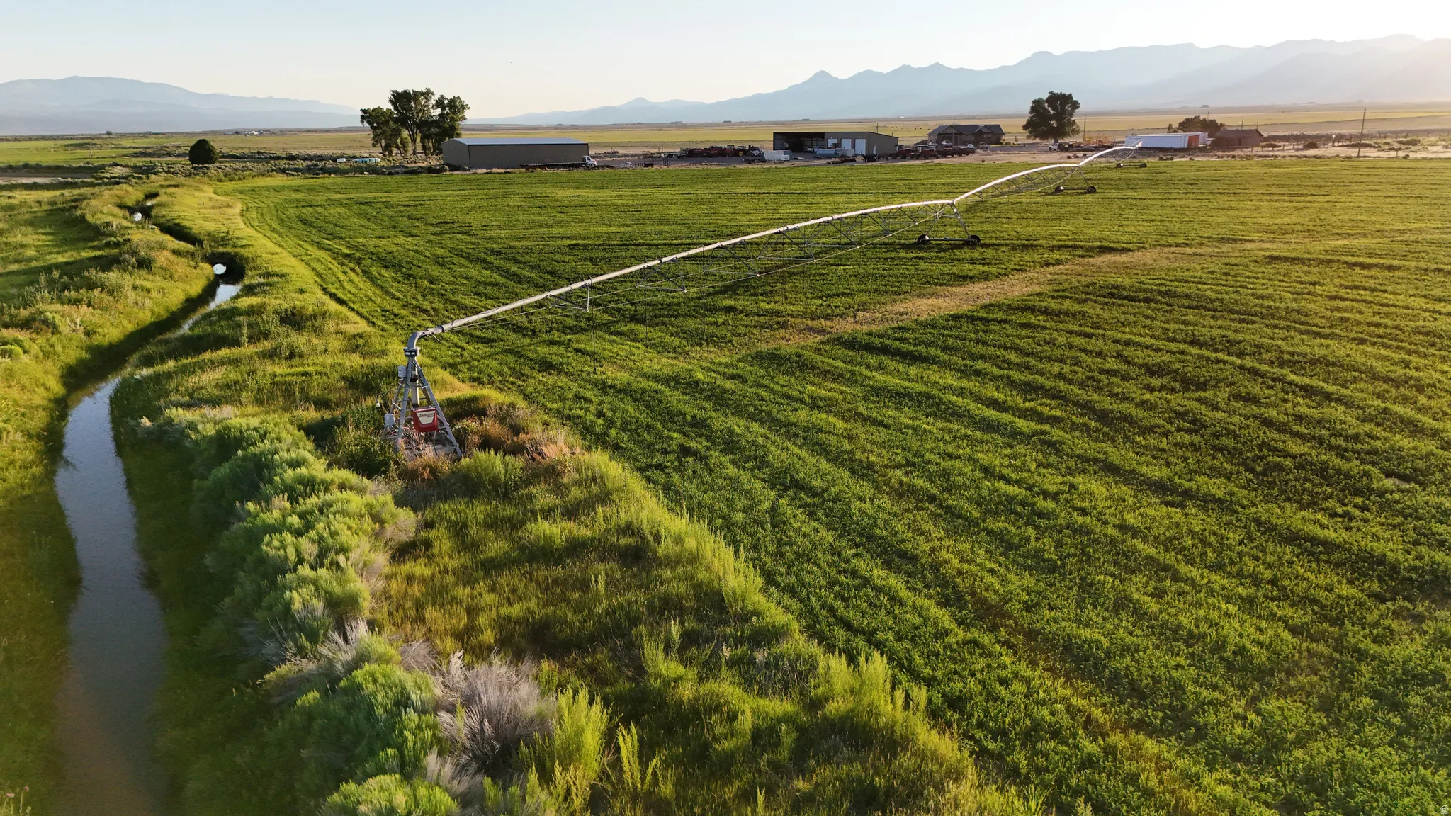 Expansive agricultural fields with irrigation system, bordered by a natural water canal