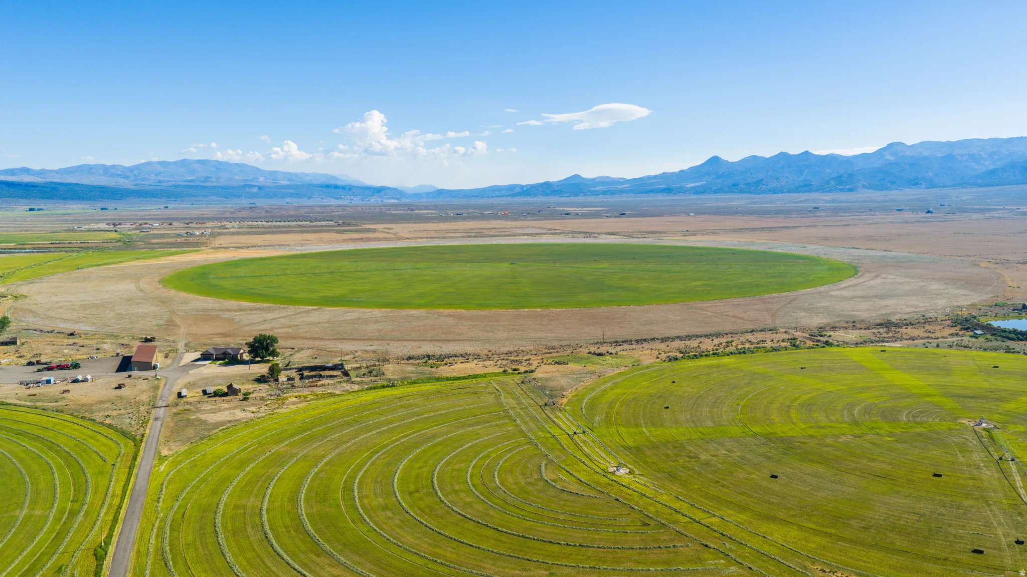 Expansive agricultural landscape featuring circular fields, distant mountains, and a clear blue sky