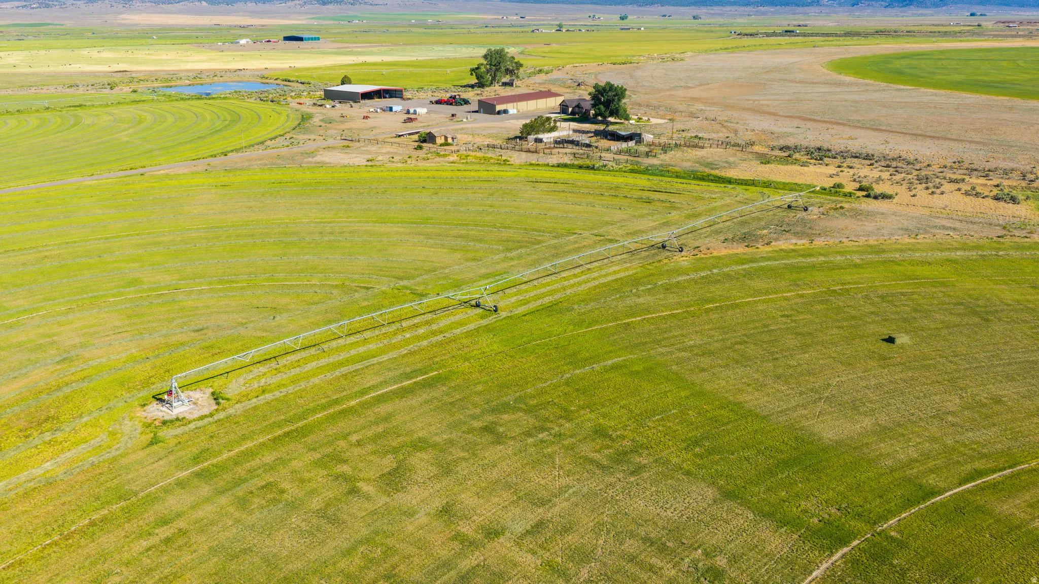 Expansive agricultural property featuring cultivated fields, irrigation systems, multiple outbuildings, and a serene pond