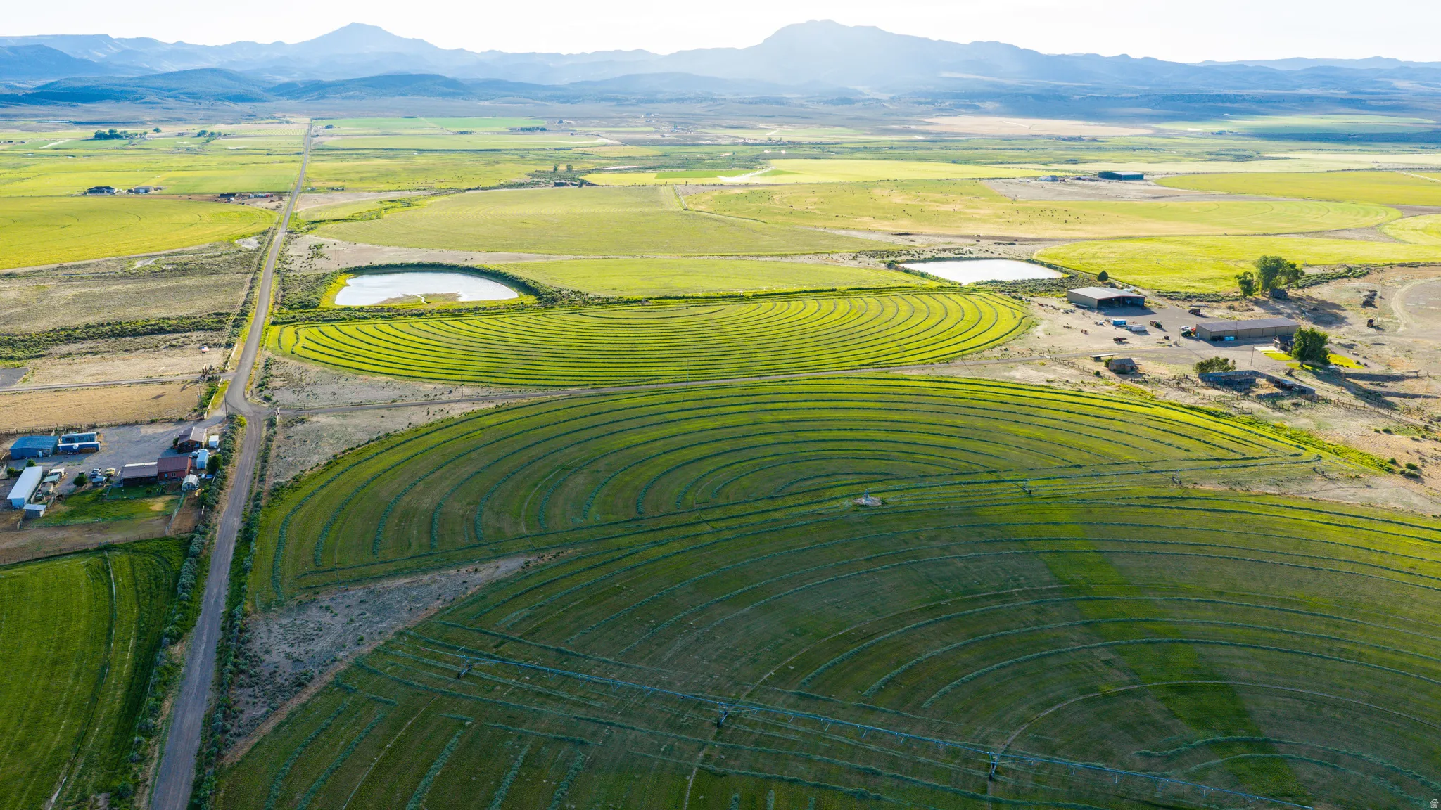 Expansive agricultural land featuring circular crop fields, a water retention pond, and distant mountains