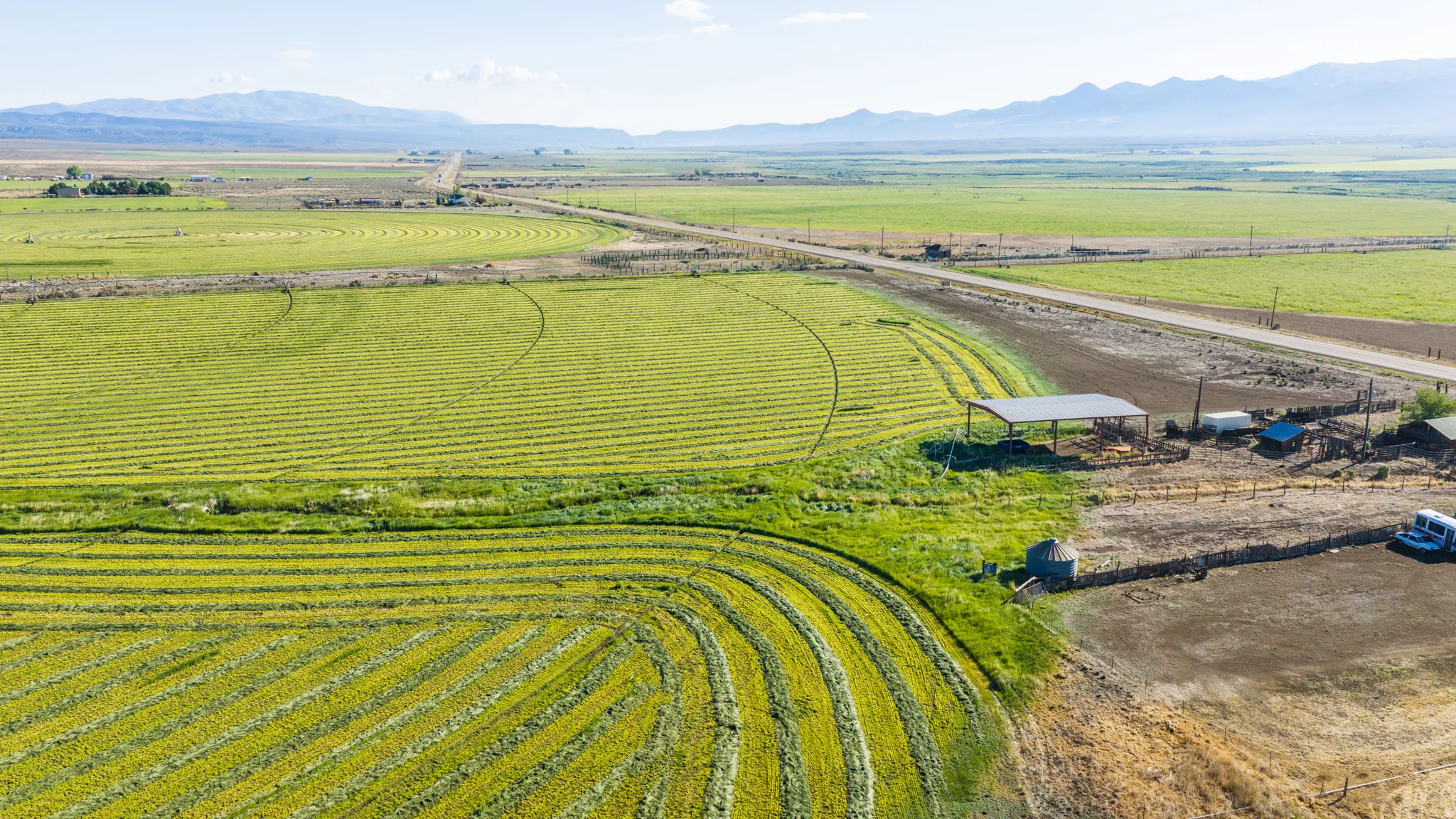 Expansive cultivated fields, barn structure, unpaved road access, mountainous backdrop, and clear sky