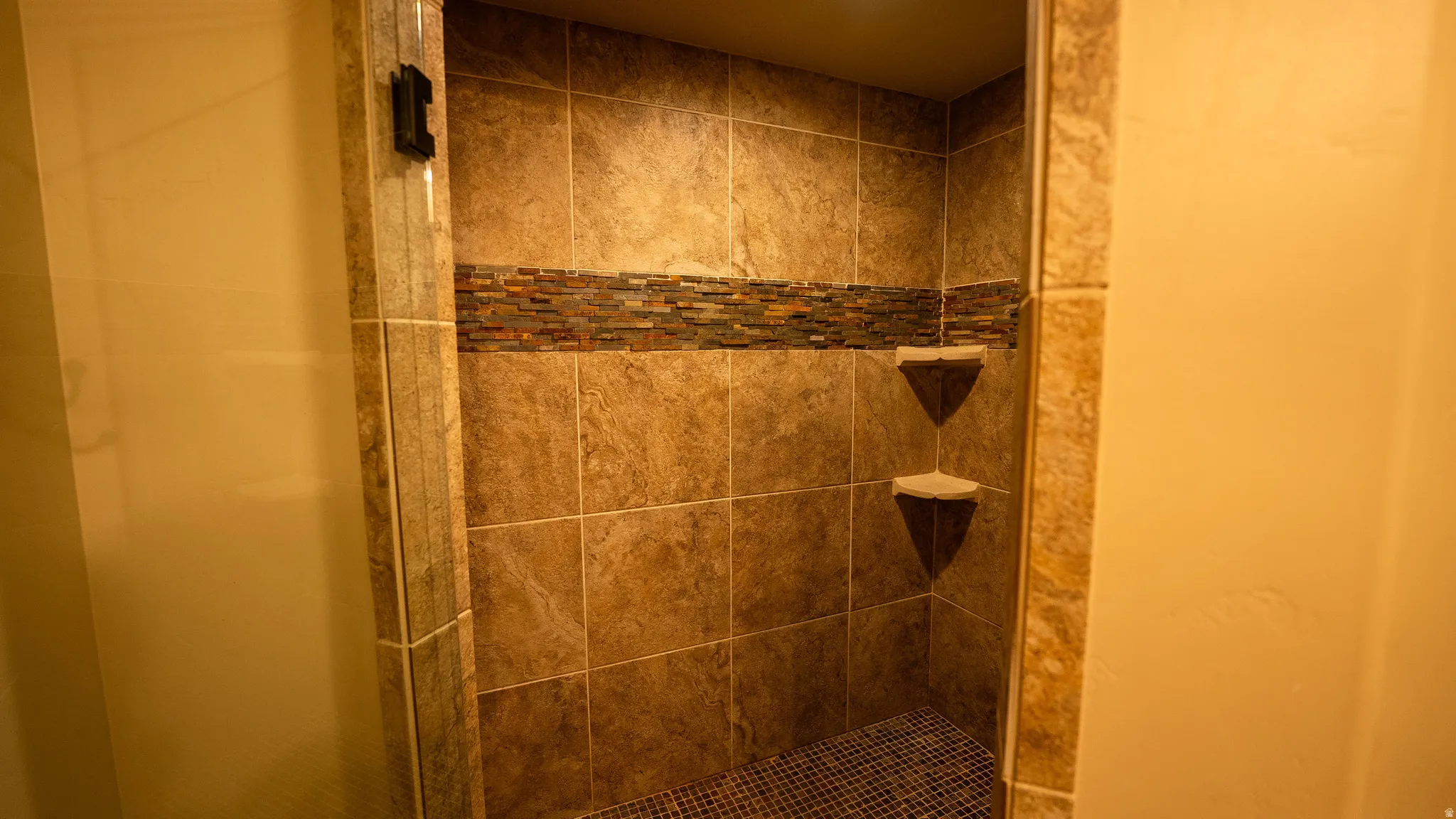 Tiled shower enclosure featuring a decorative mosaic accent band and two built-in corner shelves