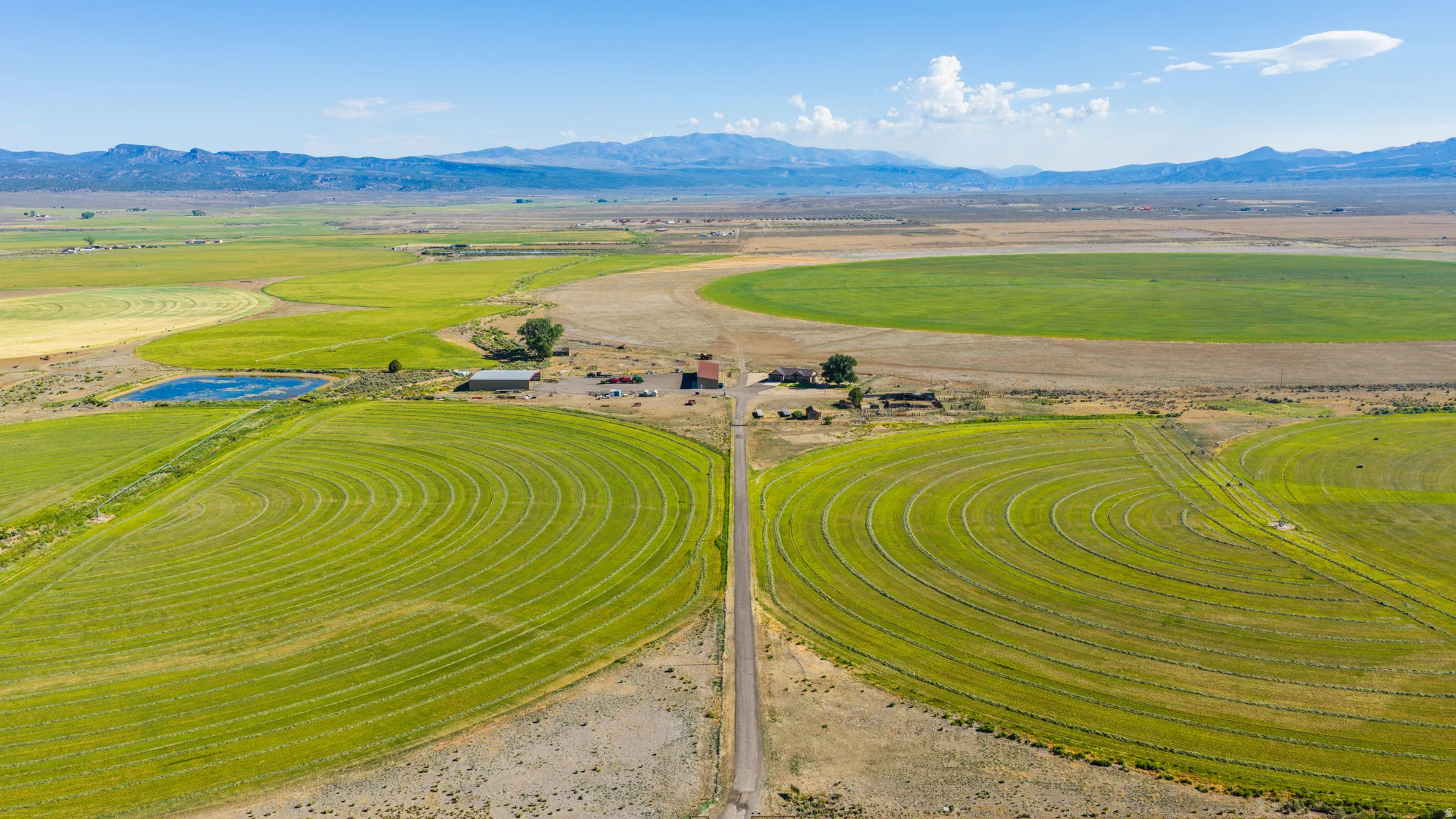 Expansive agricultural property featuring multiple cultivated fields, a private pond, and distant mountain ranges