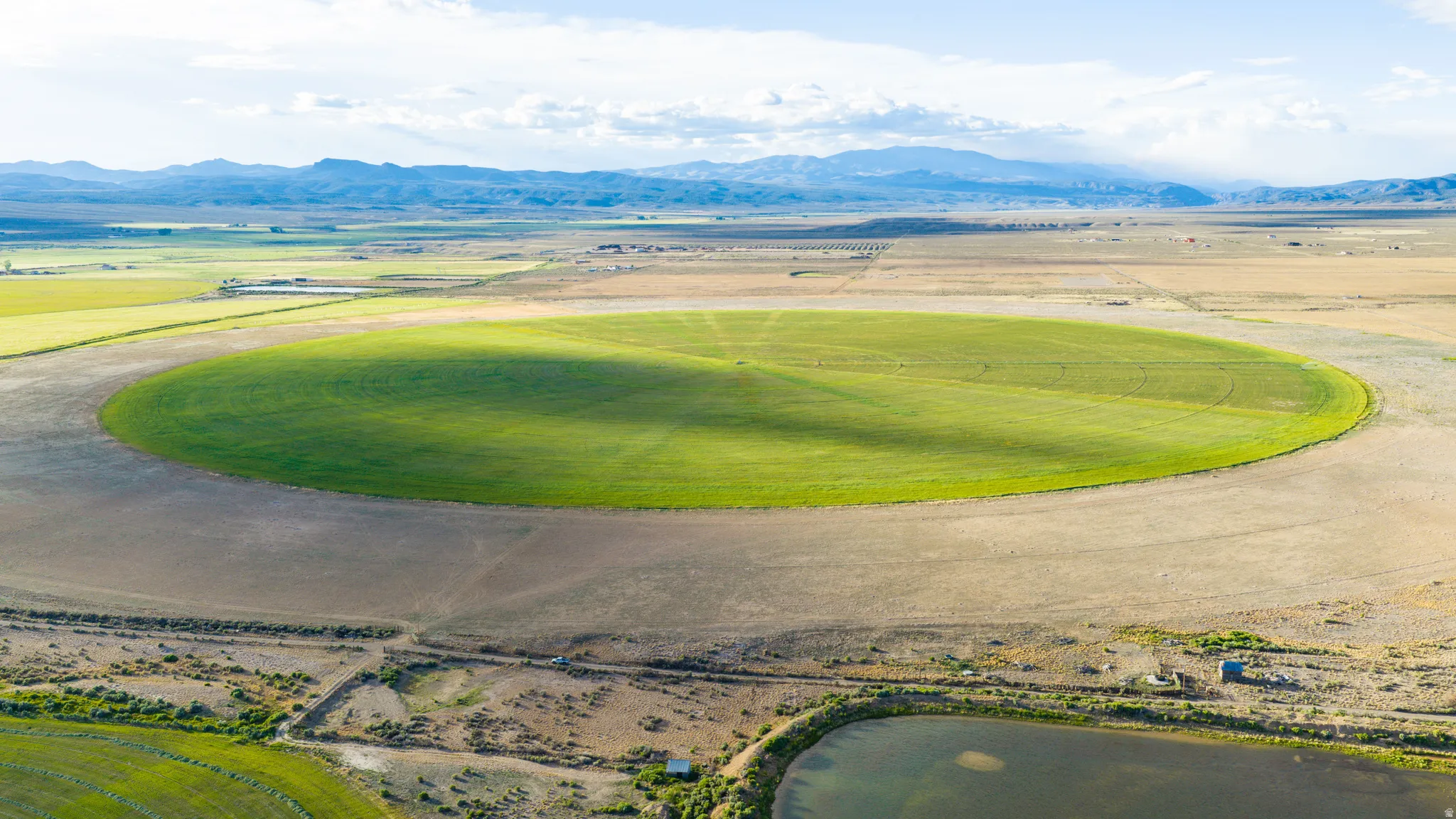 Expansive agricultural land featuring a large circular field, surrounding undeveloped terrain, and distant mountain ranges