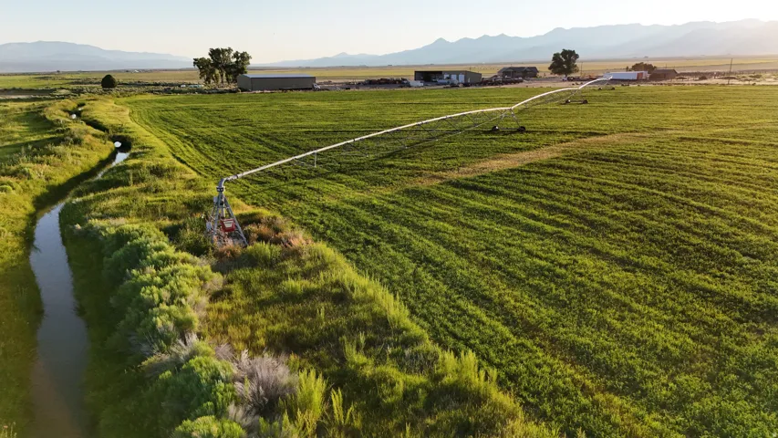 Expansive agricultural fields with irrigation system, bordered by a natural water canal
