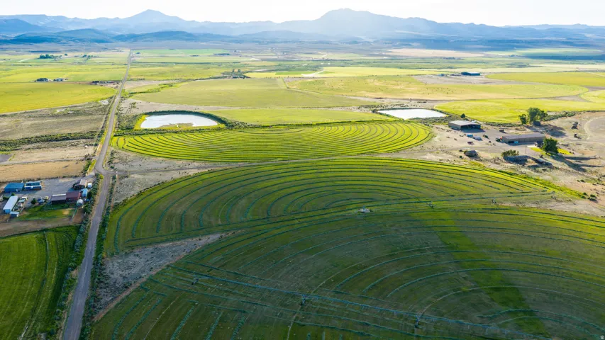 Expansive agricultural land featuring circular crop fields, a water retention pond, and distant mountains