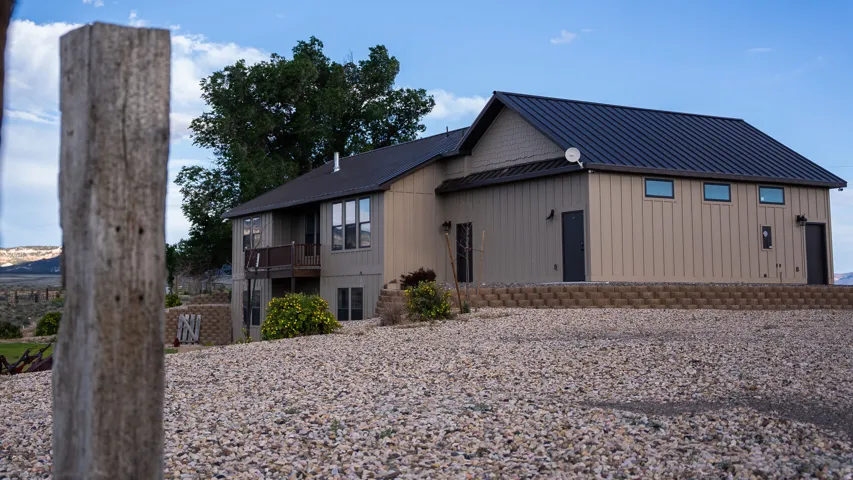 Multi-level exterior with a dark metal roof, featuring a balcony, multiple windows, and a gravel-covered ground