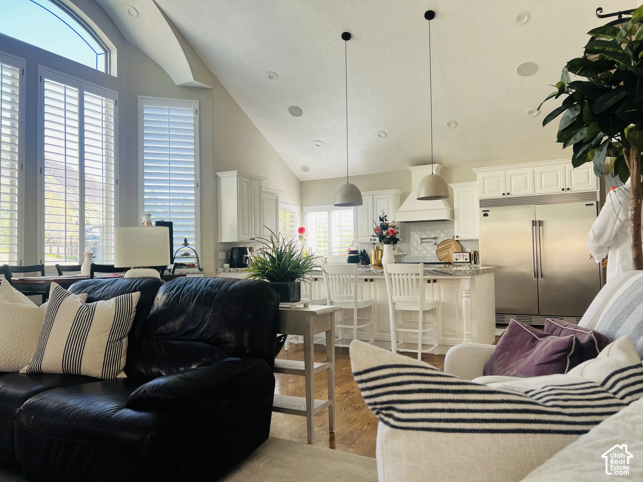 Vaulted ceiling, recessed lighting, wood-finish flooring, white plantation shutters, and a kitchen with stainless steel appliances