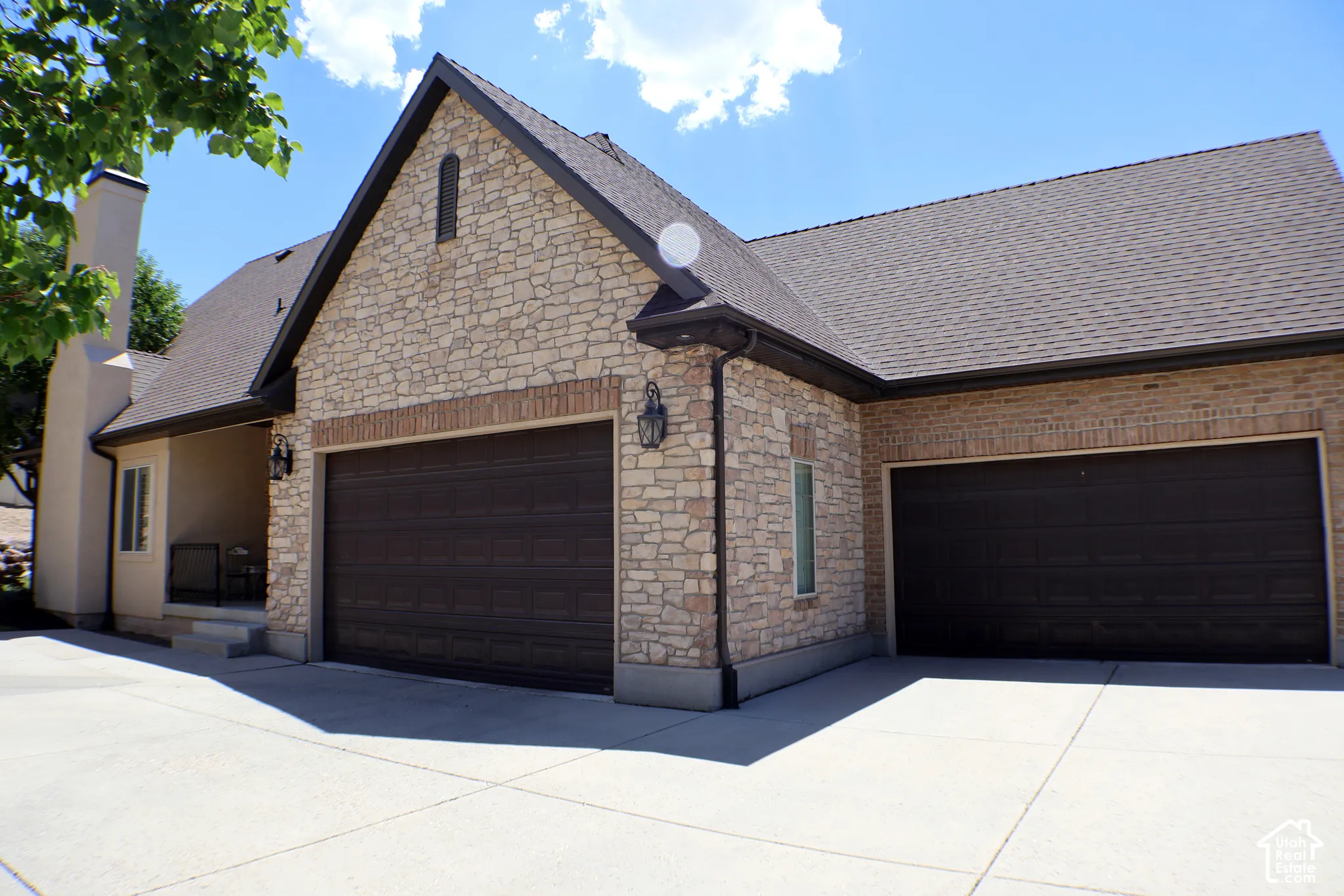 Stone and brick facade with multiple garage doors, concrete driveway, and a covered porch
