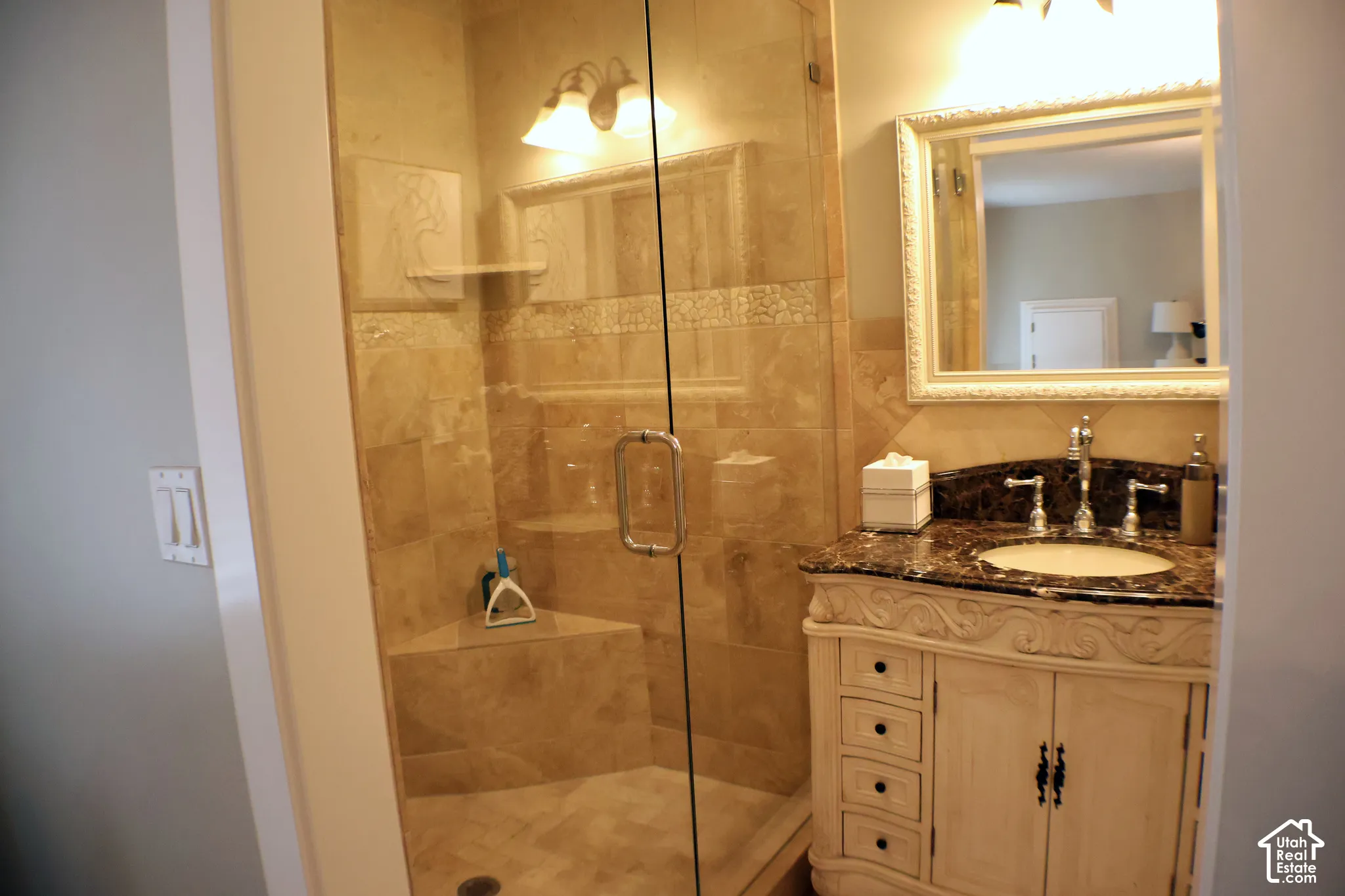 Glass-enclosed shower with stone tile, built-in shelving, and a decorative vanity with a stone countertop