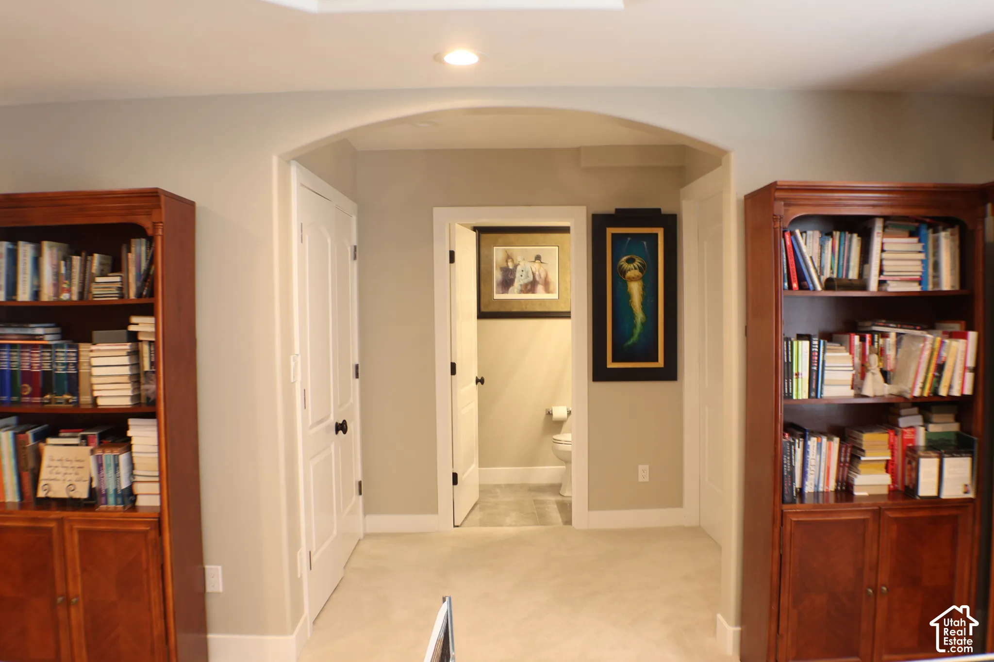 Recessed ceiling lighting, arched entryway, light-colored carpeting, two built-in storage units, and a compact bathroom with a visible toilet