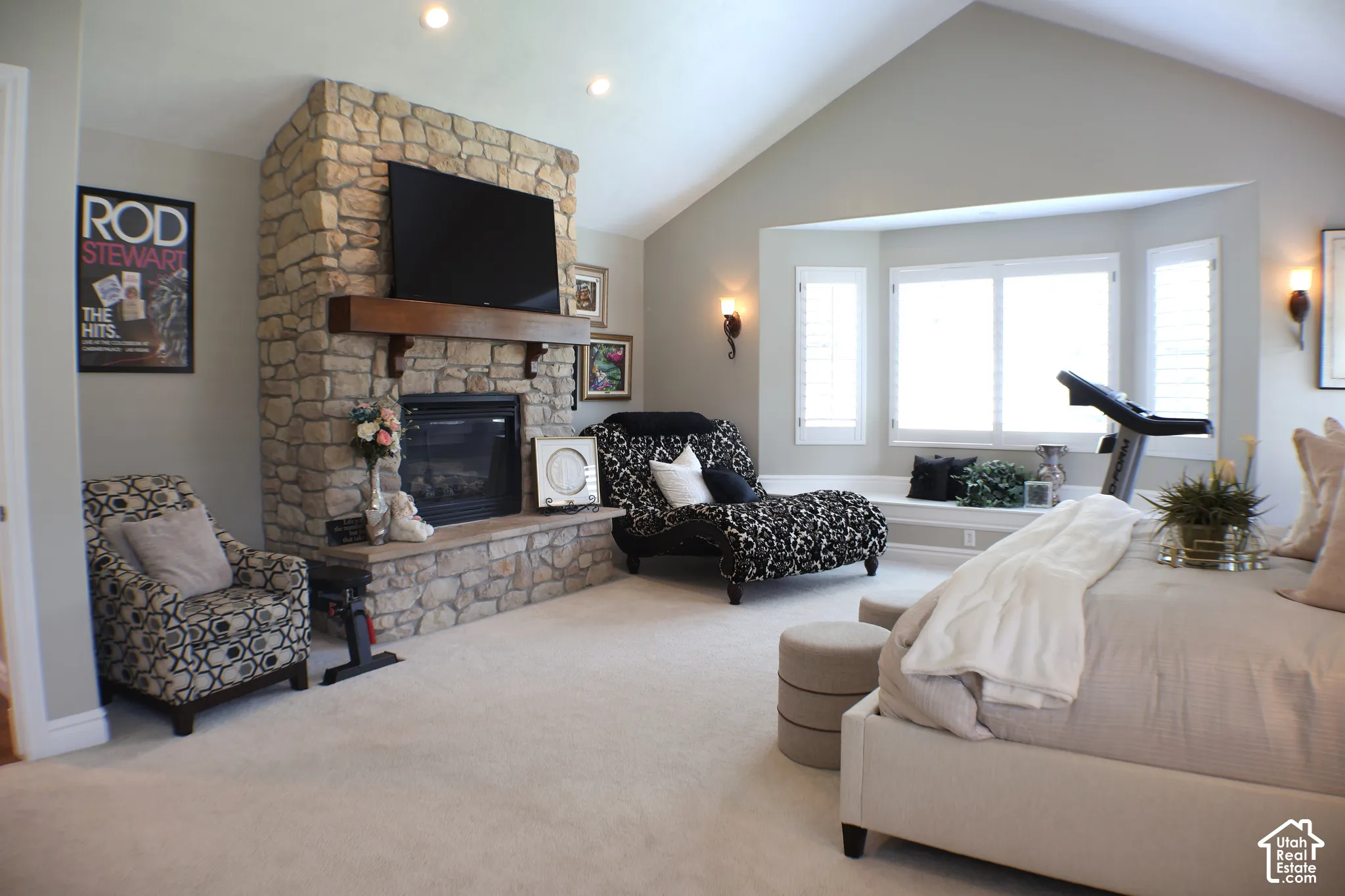 Stone-clad fireplace with a wood mantel, vaulted ceiling, bay window with built-in seating, and wall-mounted sconces