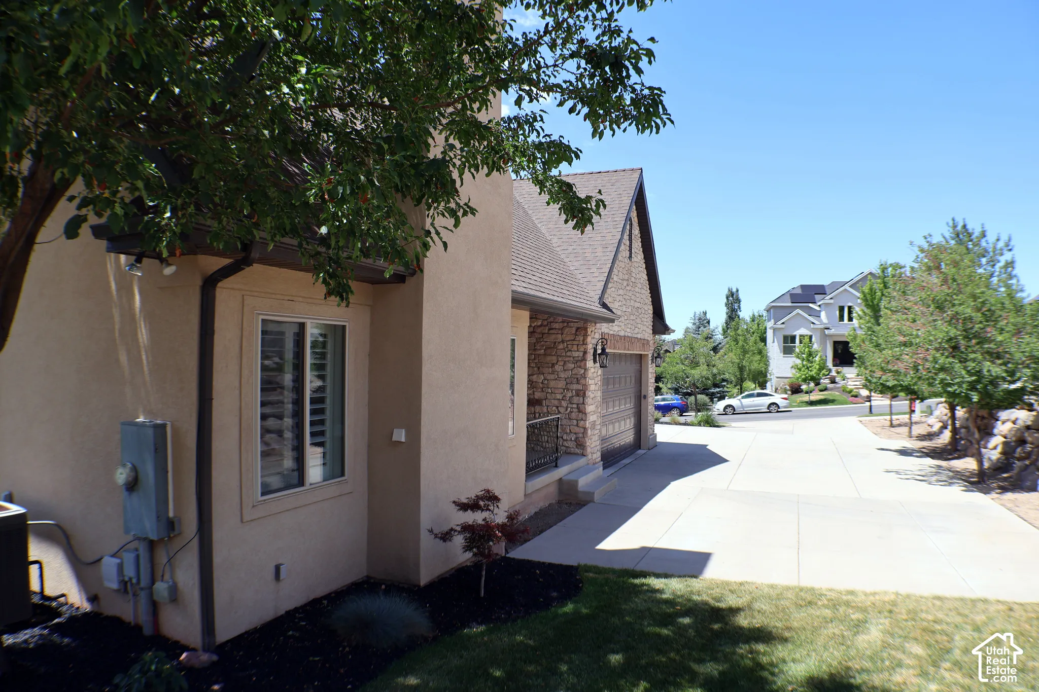 Stucco exterior, stone facade accents, concrete driveway, attached garage, and mature landscaping