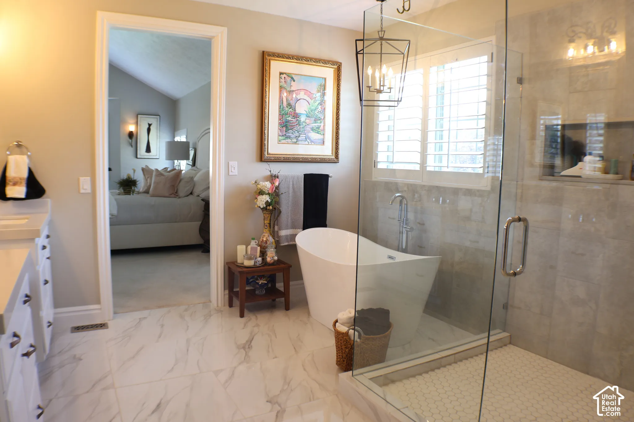 Freestanding soaking tub with floor-mounted faucet, glass-enclosed shower featuring a mosaic tile pan, shuttered window, and large format marble-look tile flooring