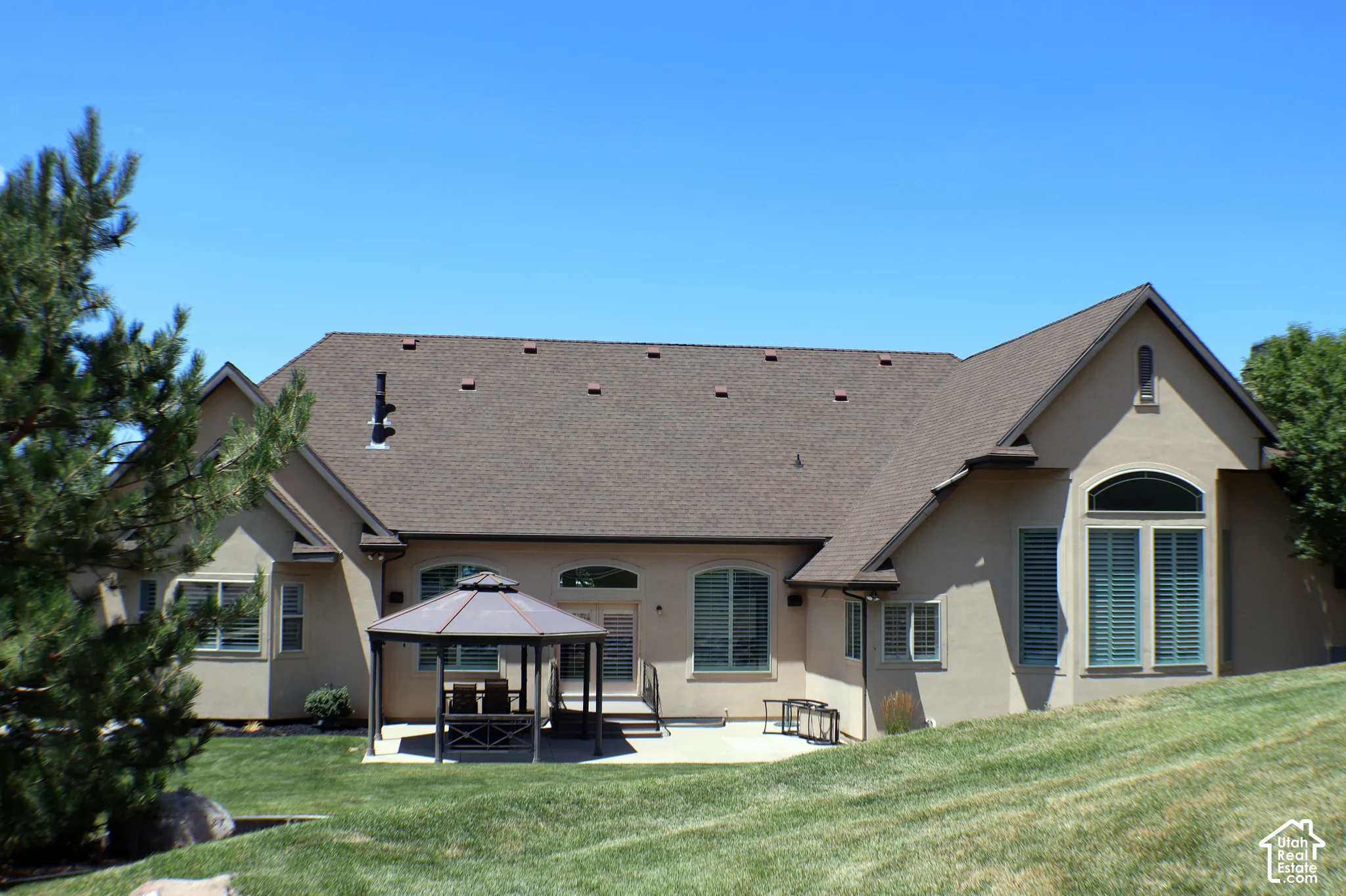 Stucco exterior with multi-pitched roofline, expansive lawn, and concrete patio