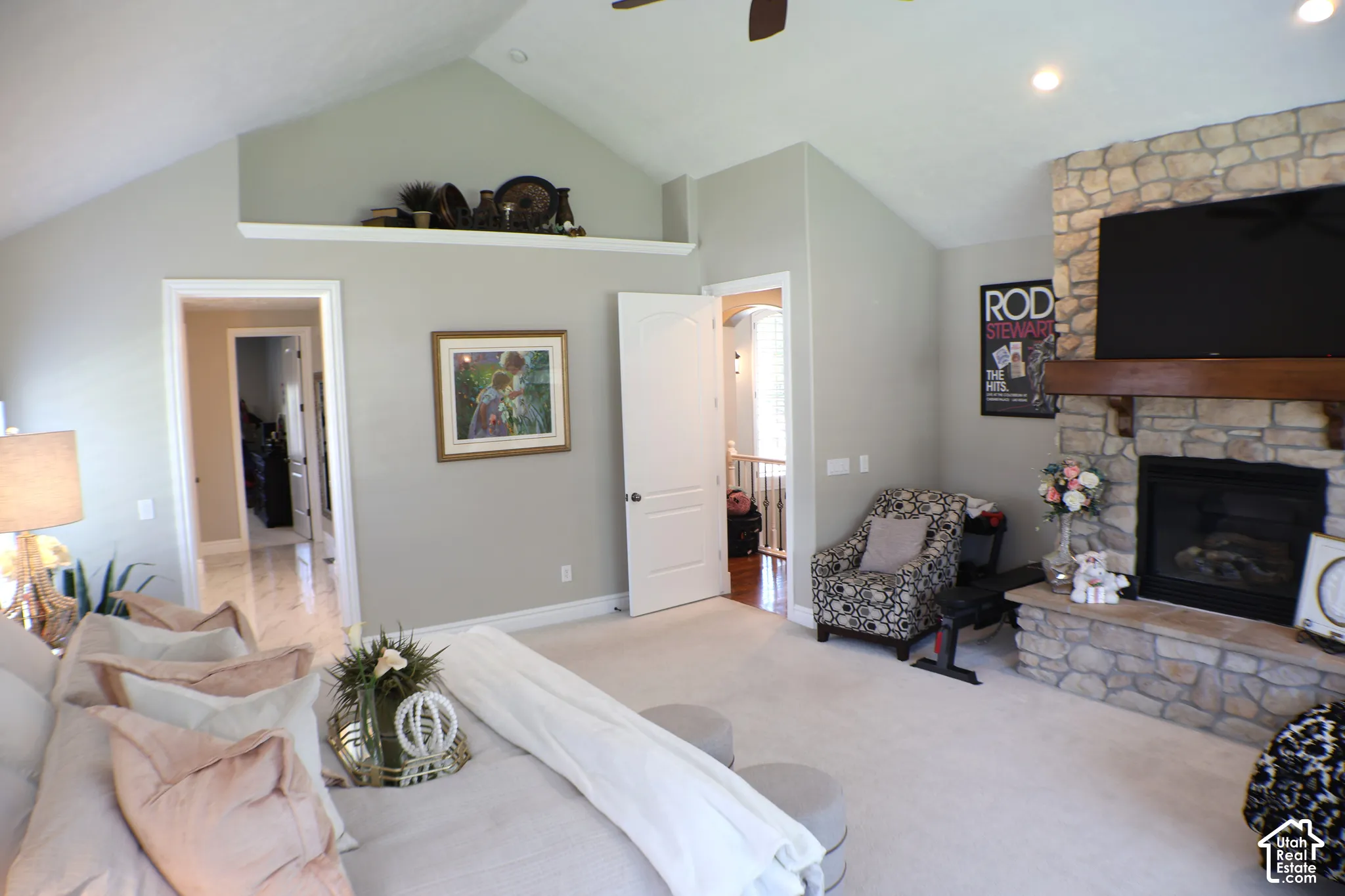 Vaulted ceiling with a display ledge, recessed lighting, stone-clad fireplace with a wood mantel, and broad doorways
