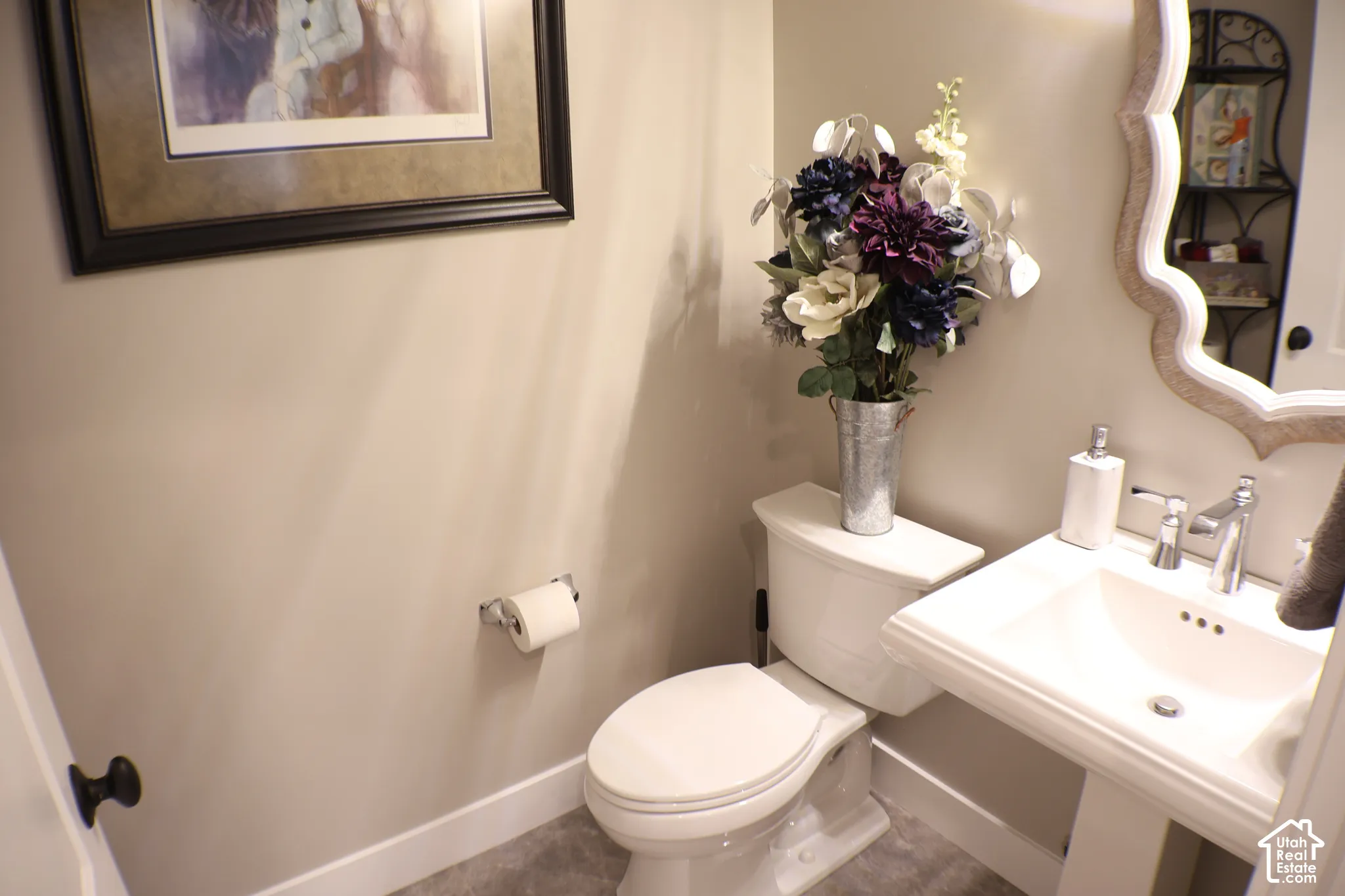 Pedestal sink with chrome faucet, white toilet, and decorative wall mirror