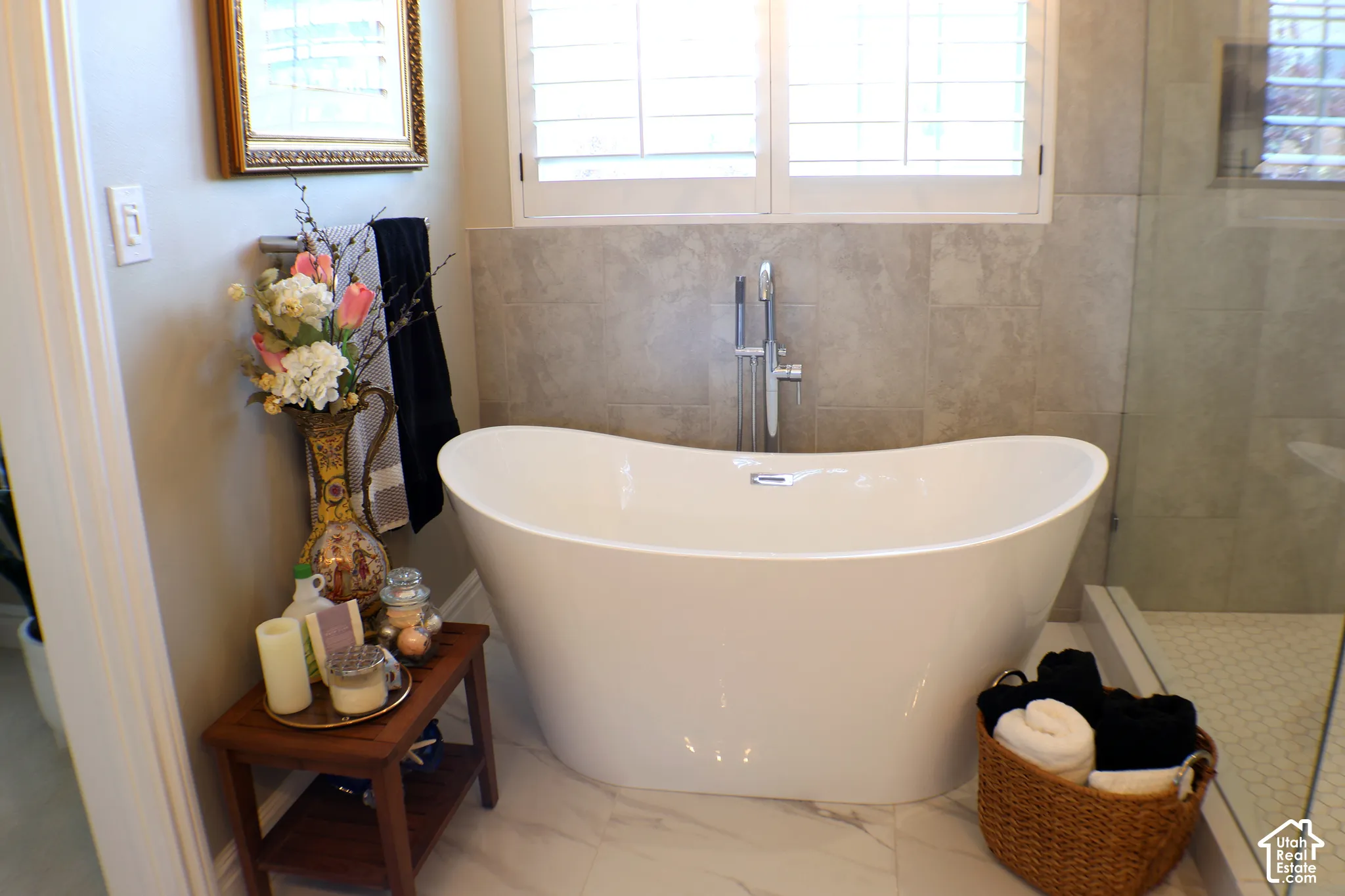 Freestanding soaking tub with polished chrome fixtures, surrounded by light-toned wall tile