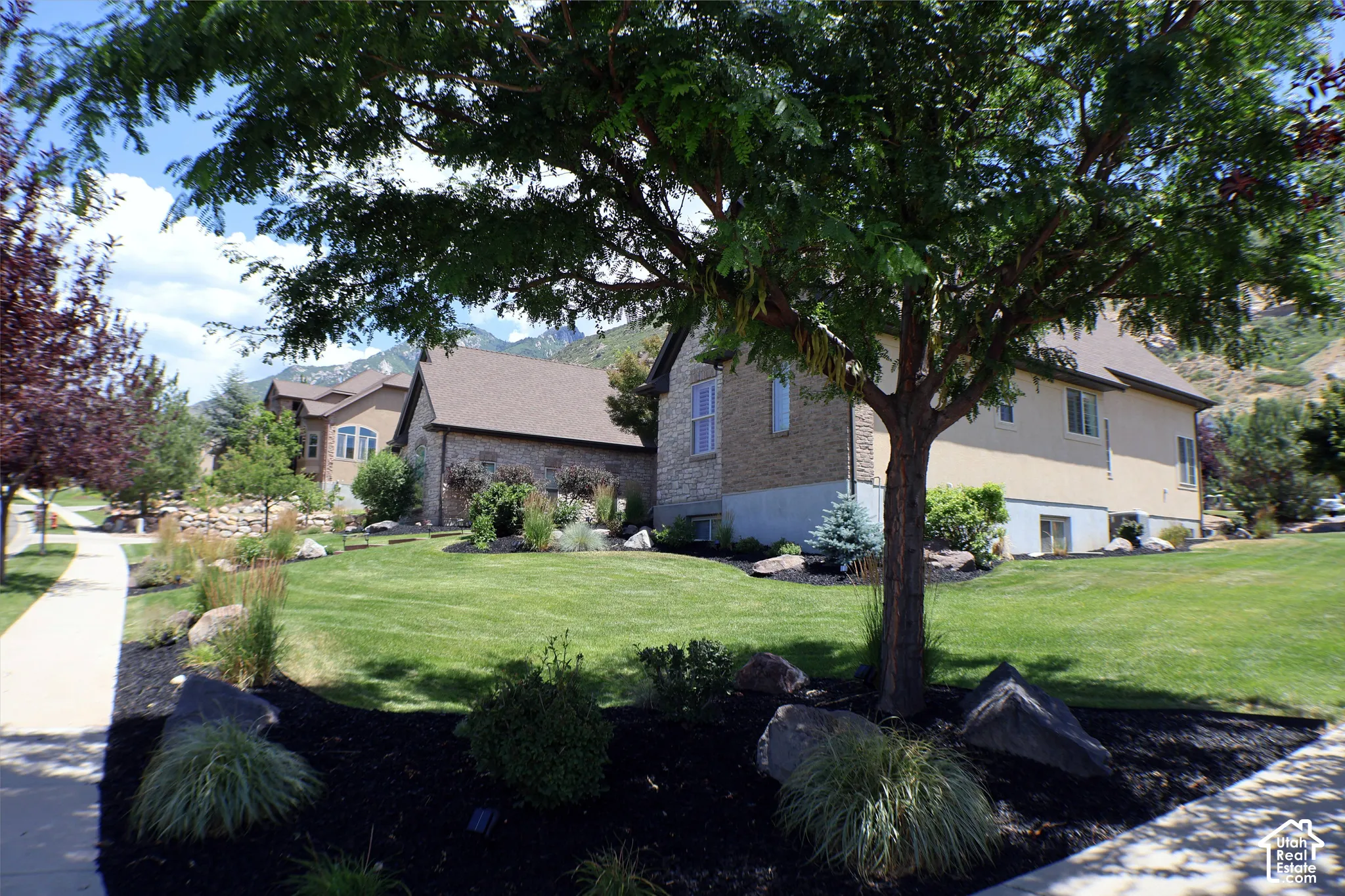 Manicured lawn with mature trees, stone and stucco exterior, and mountain backdrop