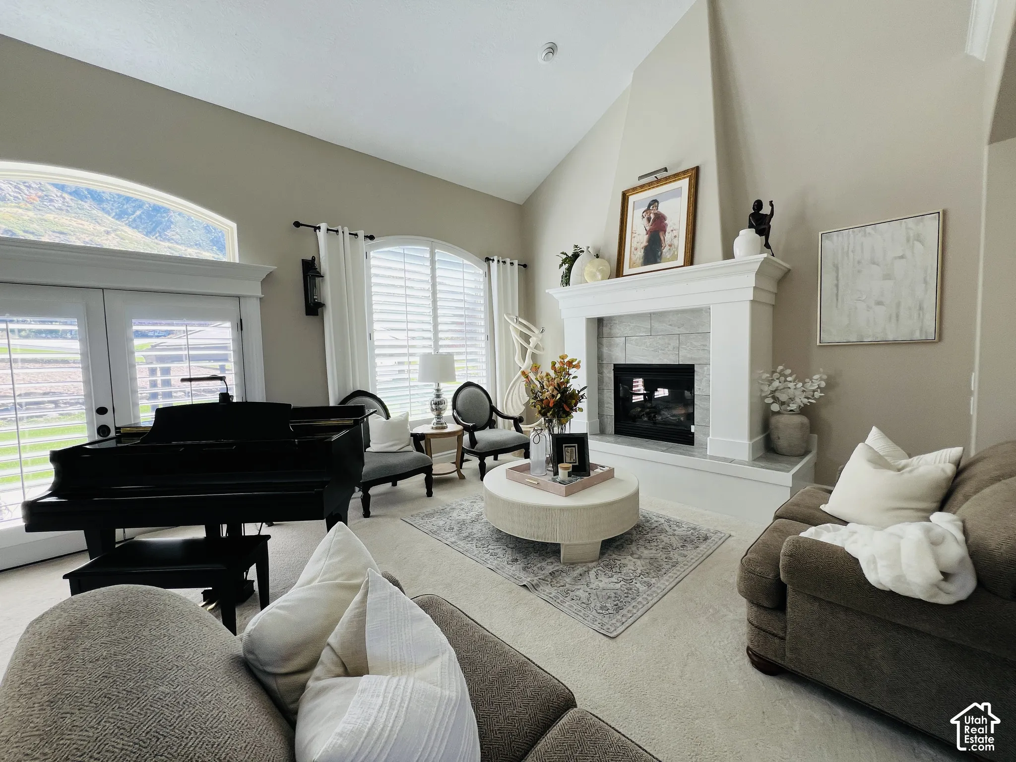 Vaulted ceilings, large arched windows, light-colored carpeting, a fireplace with a stone surround, and white plantation shutters