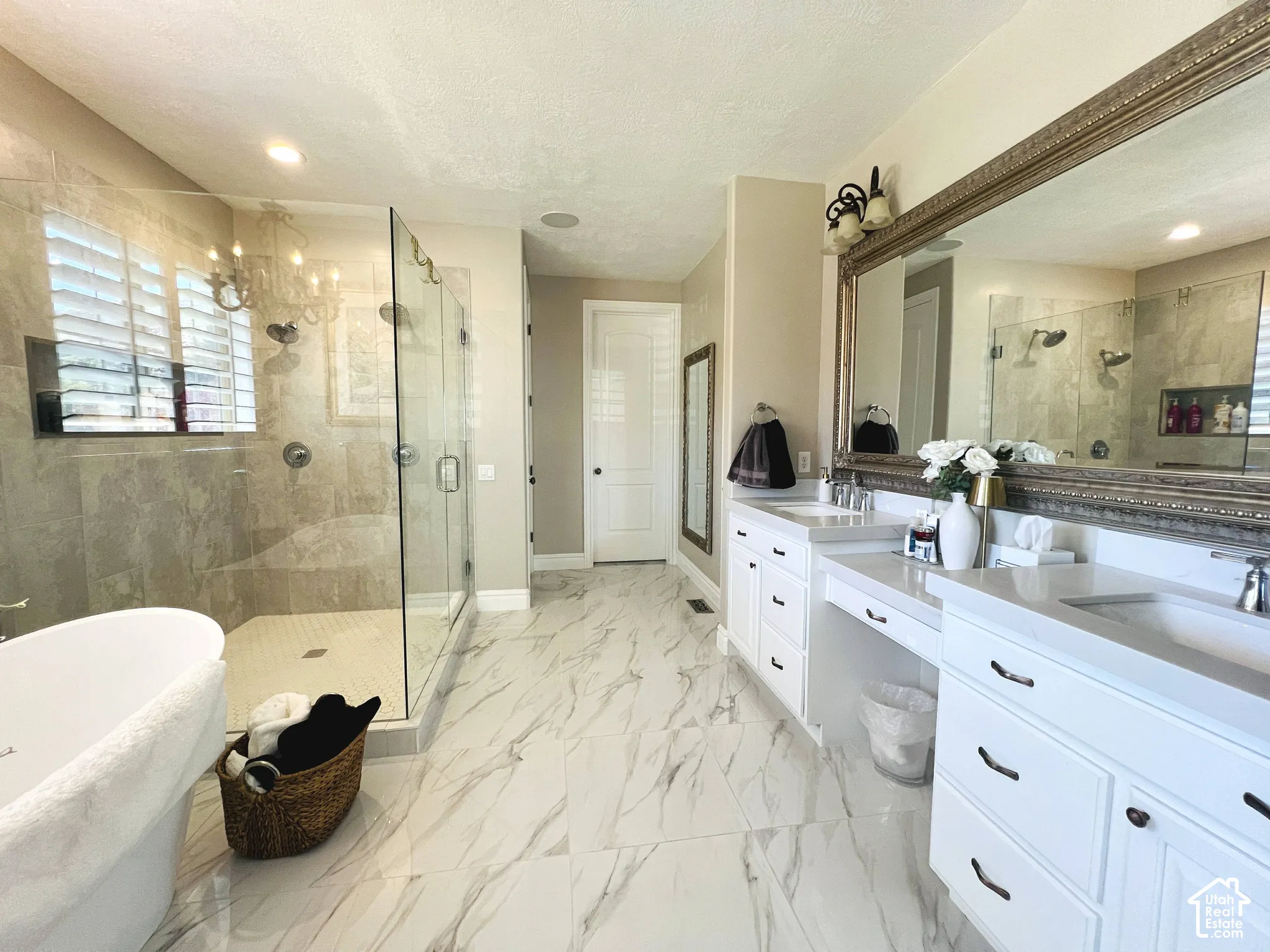 Spacious bathroom featuring a freestanding tub, expansive glass-enclosed shower with tiled walls, dual vanities with integrated sinks, and large-format tile flooring
