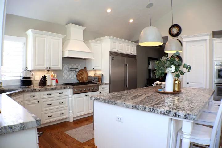 White shaker cabinetry, stainless steel appliances, patterned tile backsplash, kitchen island with stone countertop, and hardwood flooring