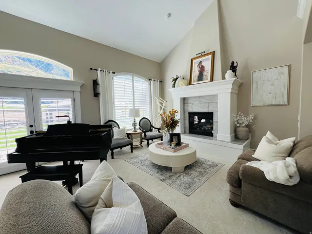 Vaulted ceilings, large arched windows, light-colored carpeting, a fireplace with a stone surround, and white plantation shutters