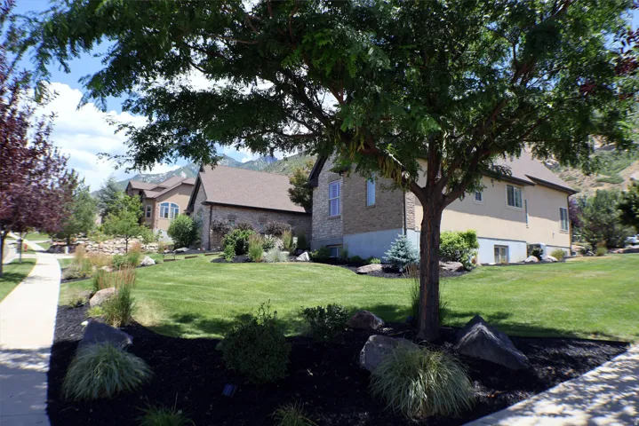 Manicured lawn with mature trees, stone and stucco exterior, and mountain backdrop