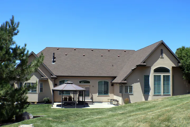 Stucco exterior with multi-pitched roofline, expansive lawn, and concrete patio