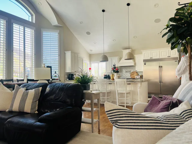 Vaulted ceiling, recessed lighting, wood-finish flooring, white plantation shutters, and a kitchen with stainless steel appliances