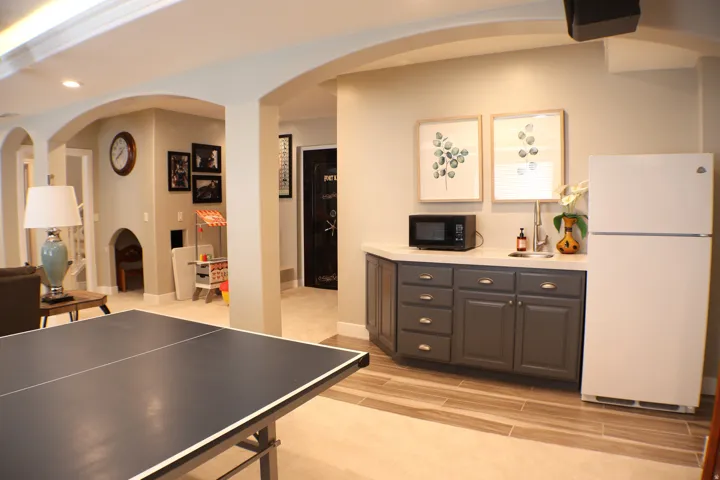 Arched doorways define the space, complemented by recessed lighting and a built-in wet bar with a countertop and sink