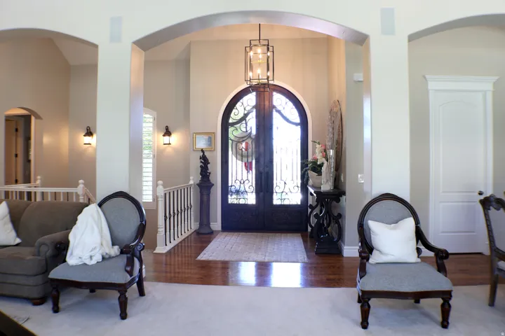 Arched entryway with a wrought iron double door, hardwood flooring, and a decorative pendant light fixture