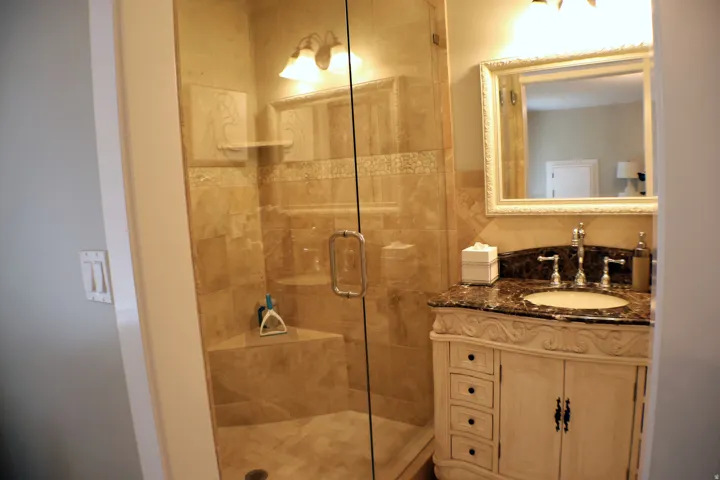 Glass-enclosed shower with stone tile, built-in shelving, and a decorative vanity with a stone countertop