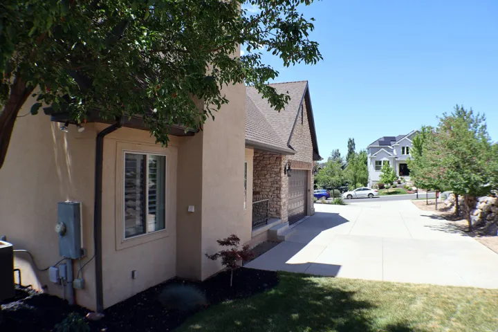 Stucco exterior, stone facade accents, concrete driveway, attached garage, and mature landscaping