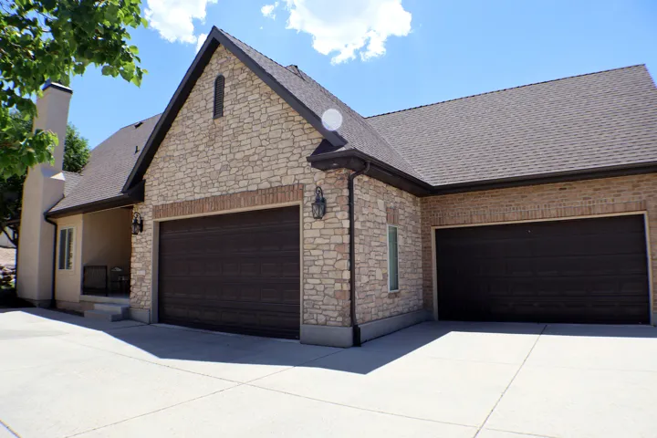 Stone and brick facade with multiple garage doors, concrete driveway, and a covered porch