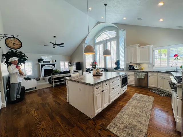 Vaulted ceilings with recessed lighting, dark wood-finish flooring, white cabinetry with dark hardware, a center island with integrated appliances, and tall windows with plantation shutters