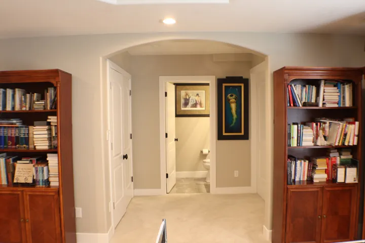 Recessed ceiling lighting, arched entryway, light-colored carpeting, two built-in storage units, and a compact bathroom with a visible toilet
